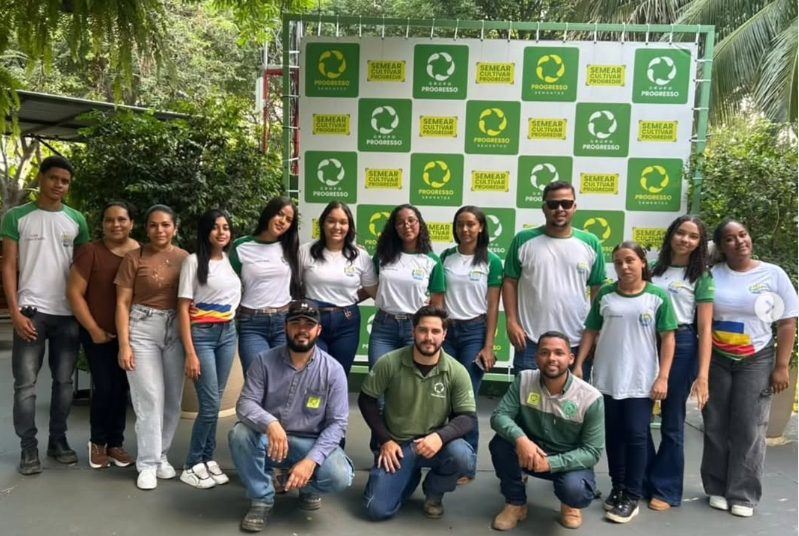 Grupo de estudantes e profissionais posando diante de um painel do Grupo Progresso e da Progresso Sementes.