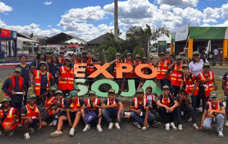 Grupo de crianças da Brigada Ambiental Mirim, de colete laranja e boné verde, posando junto ao letreiro "Expo Soja" na ExpoLeal.